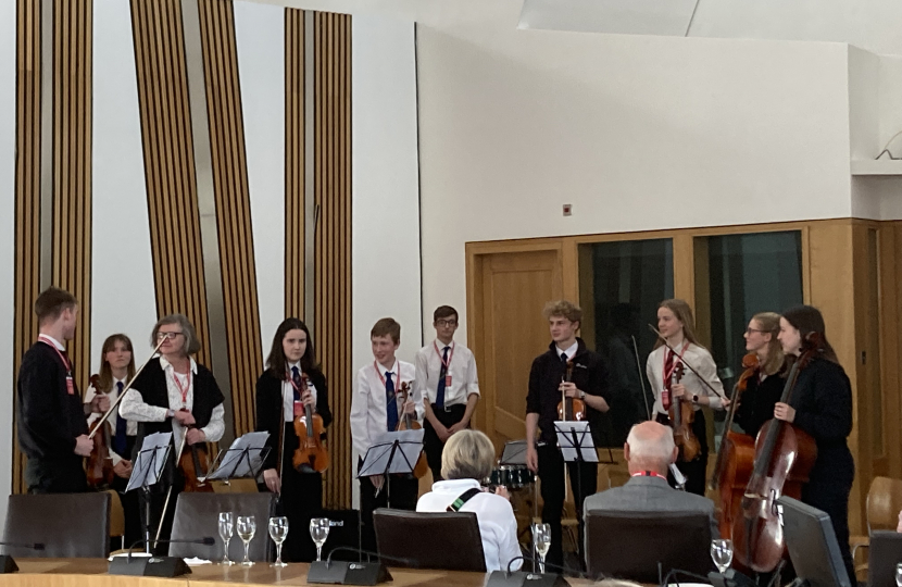 (left-to-right) Michael Hoole (Violinist), Ivy Briggs (Pianist), Pauline Hickman (Instructor-Violin), Isabella Gold (Violinist), Brodie Wallace (Violinist), Ben Gentil (Drummer), Thomas Bull (Violinist), Lois Thomson (Violinist), Freya Harley (Celloist) and Hannah Swinney (Celloist) receiving applause following their performance at Craig Hoy MSP’s Community Champions reception in the Scottish Parliament.