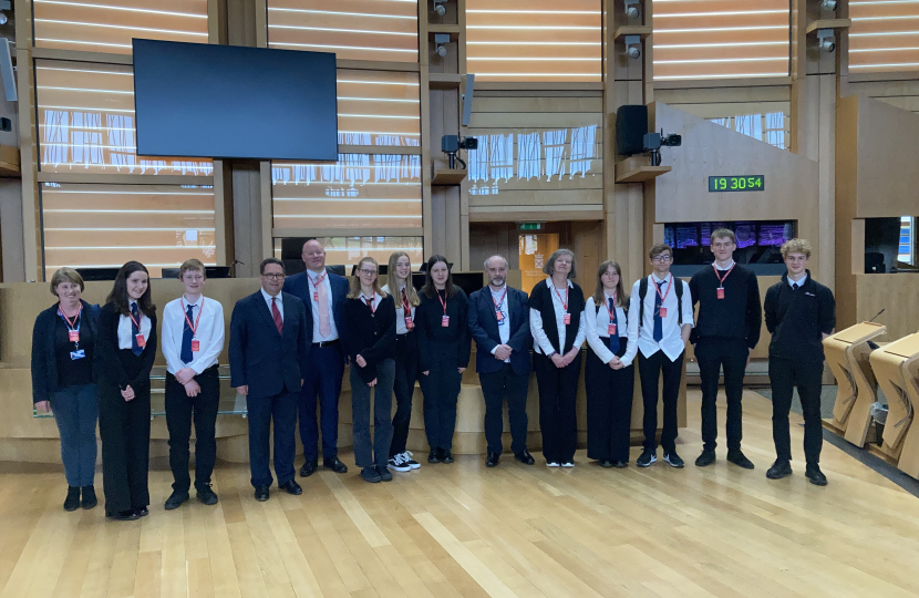 (left-to-right) Carolyn Wilson (Instructor), Isabella Gold (Violinist), Brodie Wallace (Violinist), Craig Hoy MSP, Jonathan Gwan (Team Manager at Instrumental Music Service), Freya Harley (Celloist), Lois Thomson (Violinist), Hannah Swinney (Celloist), Ewing Lauder (Instructor), Pauline Hickman (Instructor), Ivy Briggs (Pianist), Ben Gentil (Drummer), Michael Hoole (Violinist) and Thomas Bull (Violinist) in the Scottish Parliament’s Debating Chamber.