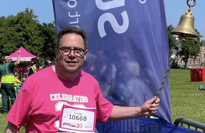 Craig Hoy MSP ringing bell at finish of Race for Life at Holyrood Park