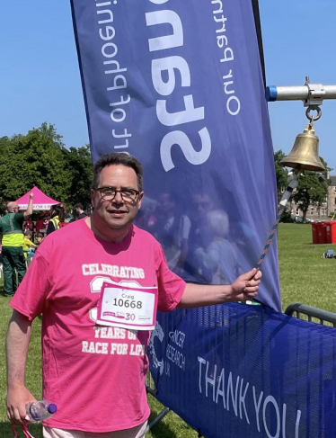 Craig Hoy MSP ringing bell at finish of Race for Life at Holyrood Park